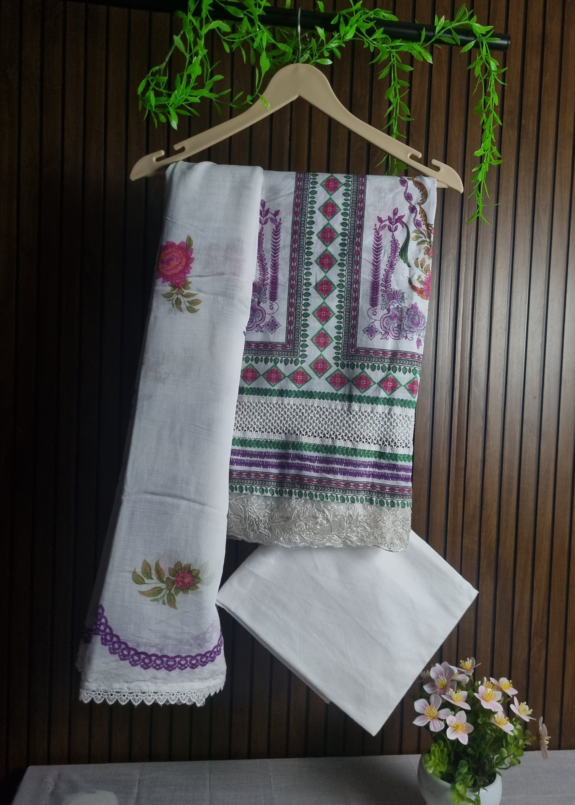 Set of embroidered towels on a wooden surface with a hanger and flowers.