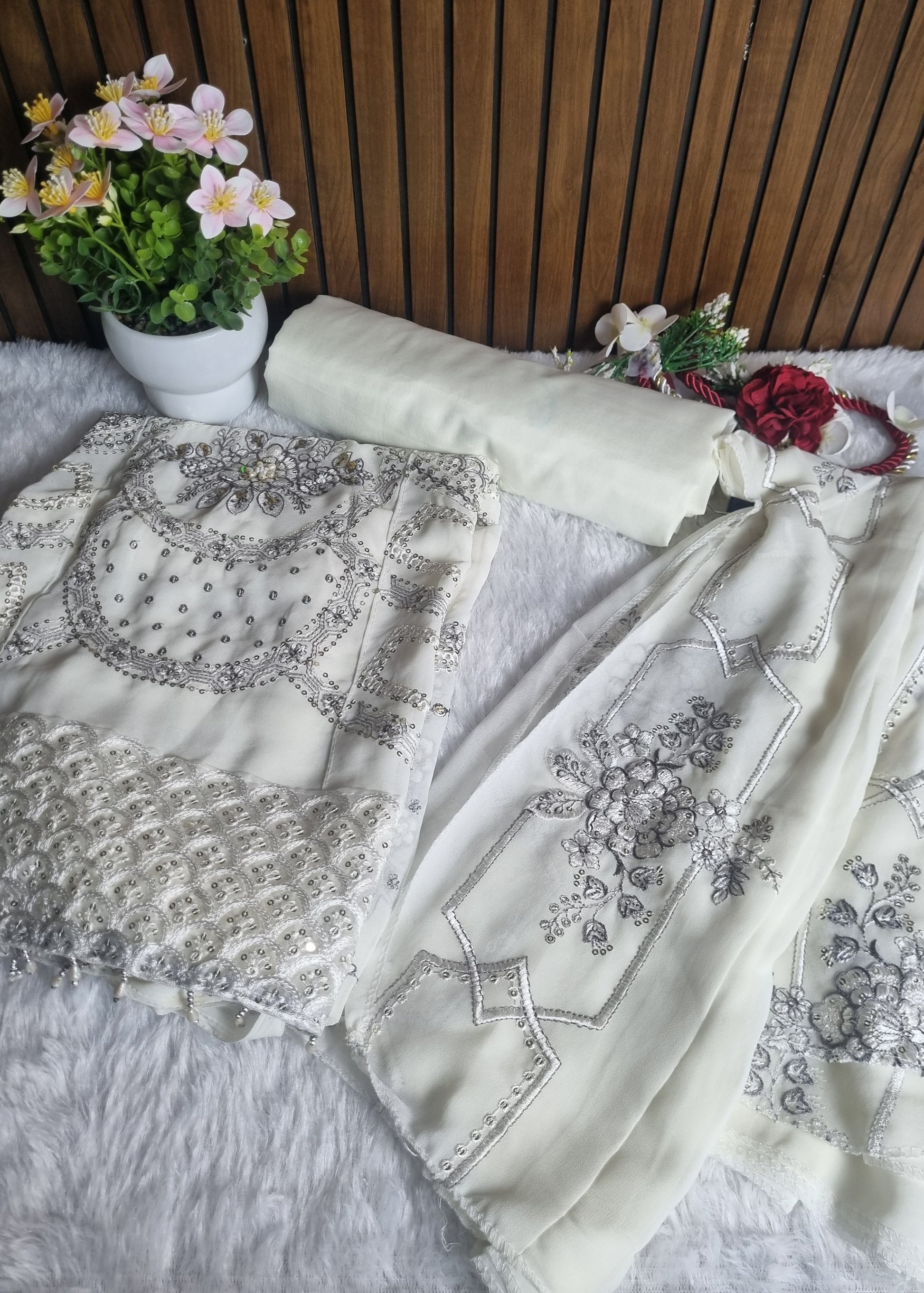 White fabric with silver embroidery on a wooden surface with flowers.