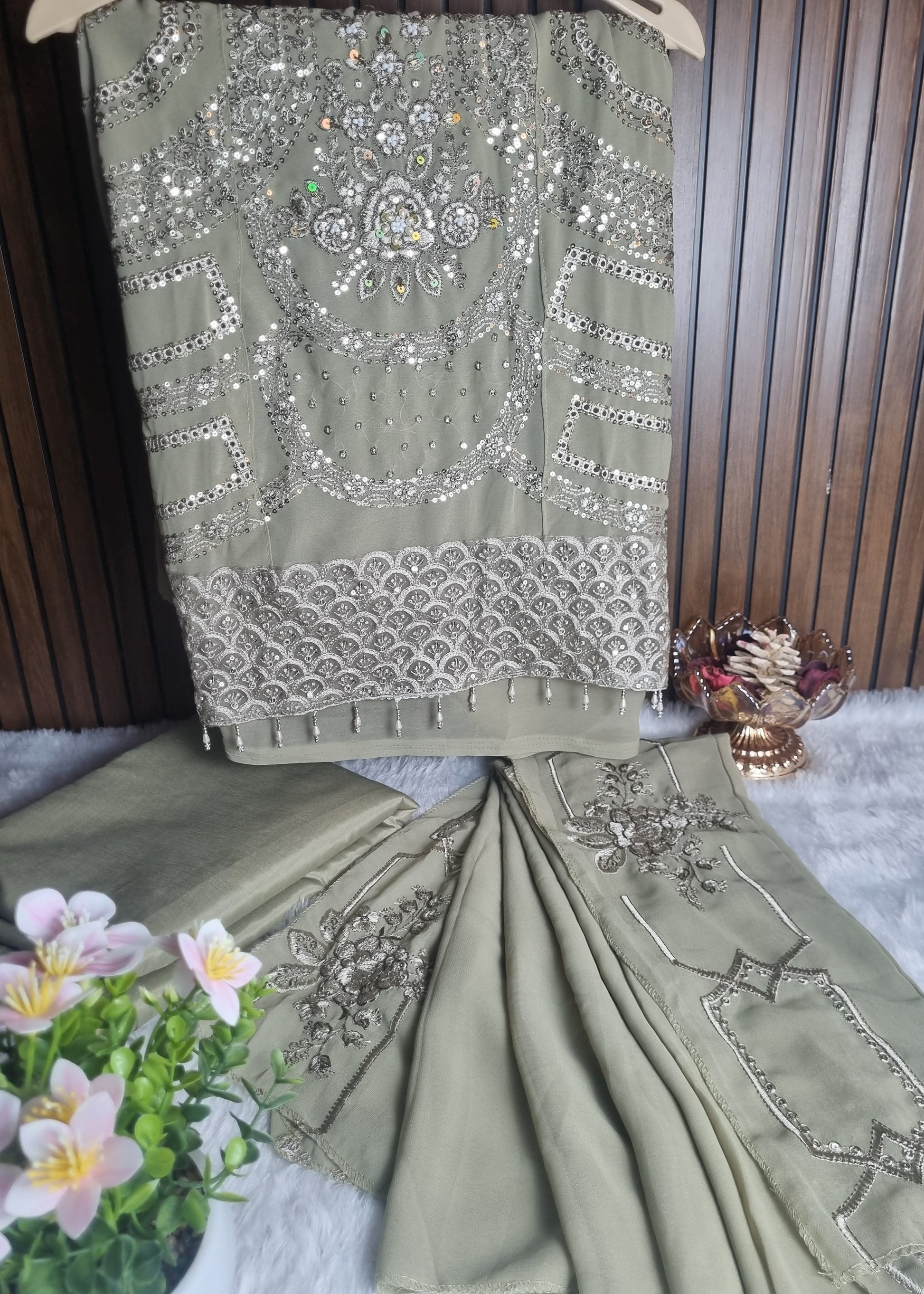Green saree with silver embroidery on a wooden surface with flowers in the background