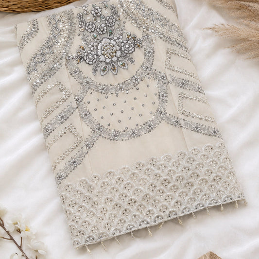 An embroidered cream-colored fabric panel with intricate silver and white beadwork, sequins, and lace borders, styled on a white satin fabric with decorative dried grass and a wicker basket.