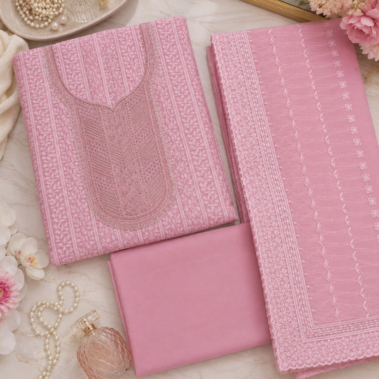 Pink embroidered traditional clothing set laid flat on a light marble surface, including a kurta with detailed embroidery, matching fabric panels, and coordinating accessories like pearls and flowers.