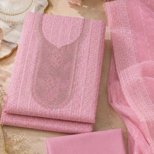 A pink traditional Indian salwar kameez fabric set with matching dupatta, featuring intricate embroidery and geometric patterns, styled in a flat-lay arrangement with decorative props.