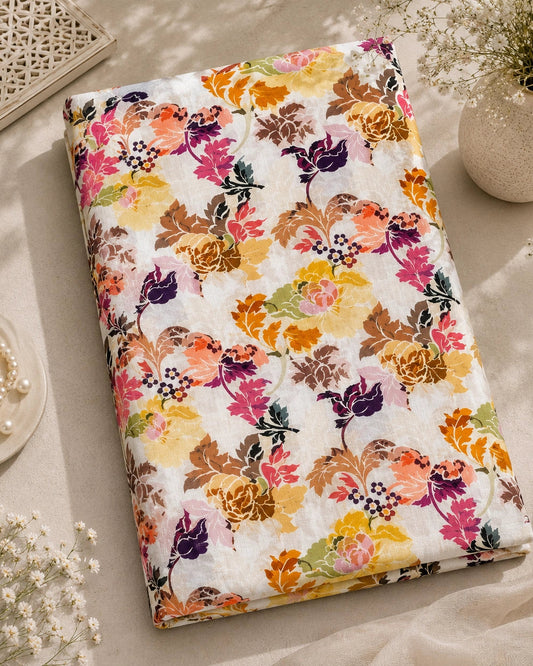 A folded fabric item, likely a quilt or blanket, featuring a vibrant multicolor floral pattern on a white background, styled in a warm, sunlit flat-lay setting with decorative props.