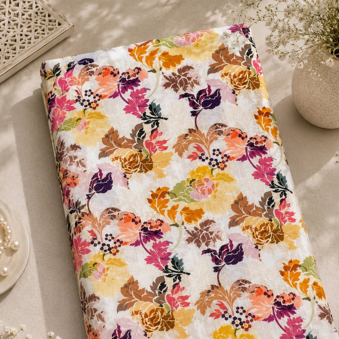 A folded fabric item, likely a quilt or blanket, featuring a vibrant multicolor floral pattern on a white background, styled in a warm, sunlit flat-lay setting with decorative props.