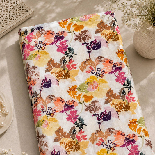 A folded fabric item, likely a quilt or blanket, featuring a vibrant multicolor floral pattern on a white background, styled in a warm, sunlit flat-lay setting with decorative props.
